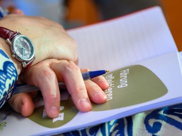 Leibniz-Akademie für Führungskräfte Hände mit Stift liegen auf einem Heft.